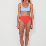 Woman wearing a light blue bikini bralette top and red high-waisted bottoms on a white background