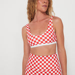 Woman wearing a red and white checkered two-piece, bralette swim top and original betty bottoms outfit on a plain background