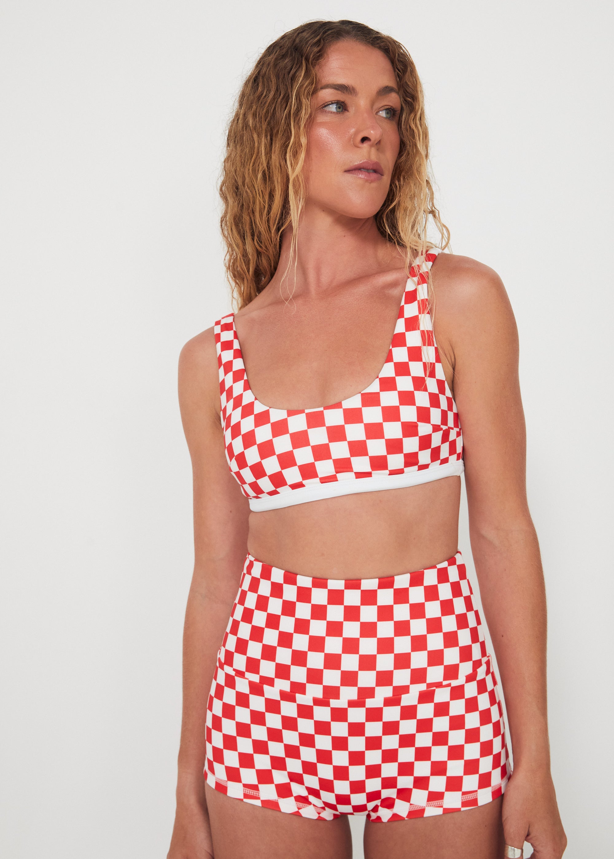Woman wearing a red and white checkered two-piece, bralette swim top and original betty bottoms outfit on a plain background