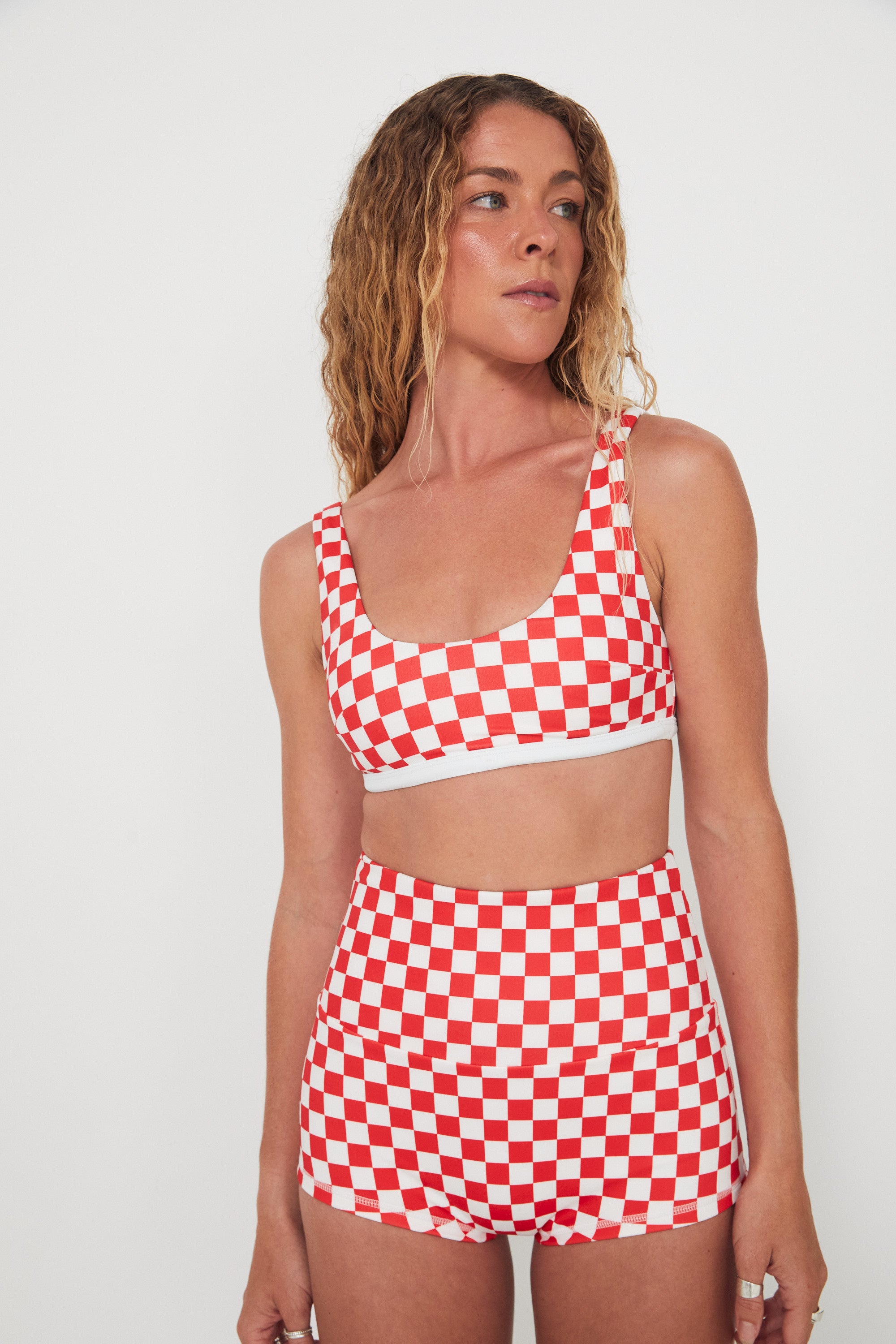 Woman wearing a red and white checkered two-piece, bralette swim top and original betty bottoms outfit on a plain background