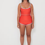 Woman wearing a red tankini surf top and betty bottoms 2.0 with blue trim on a white background
