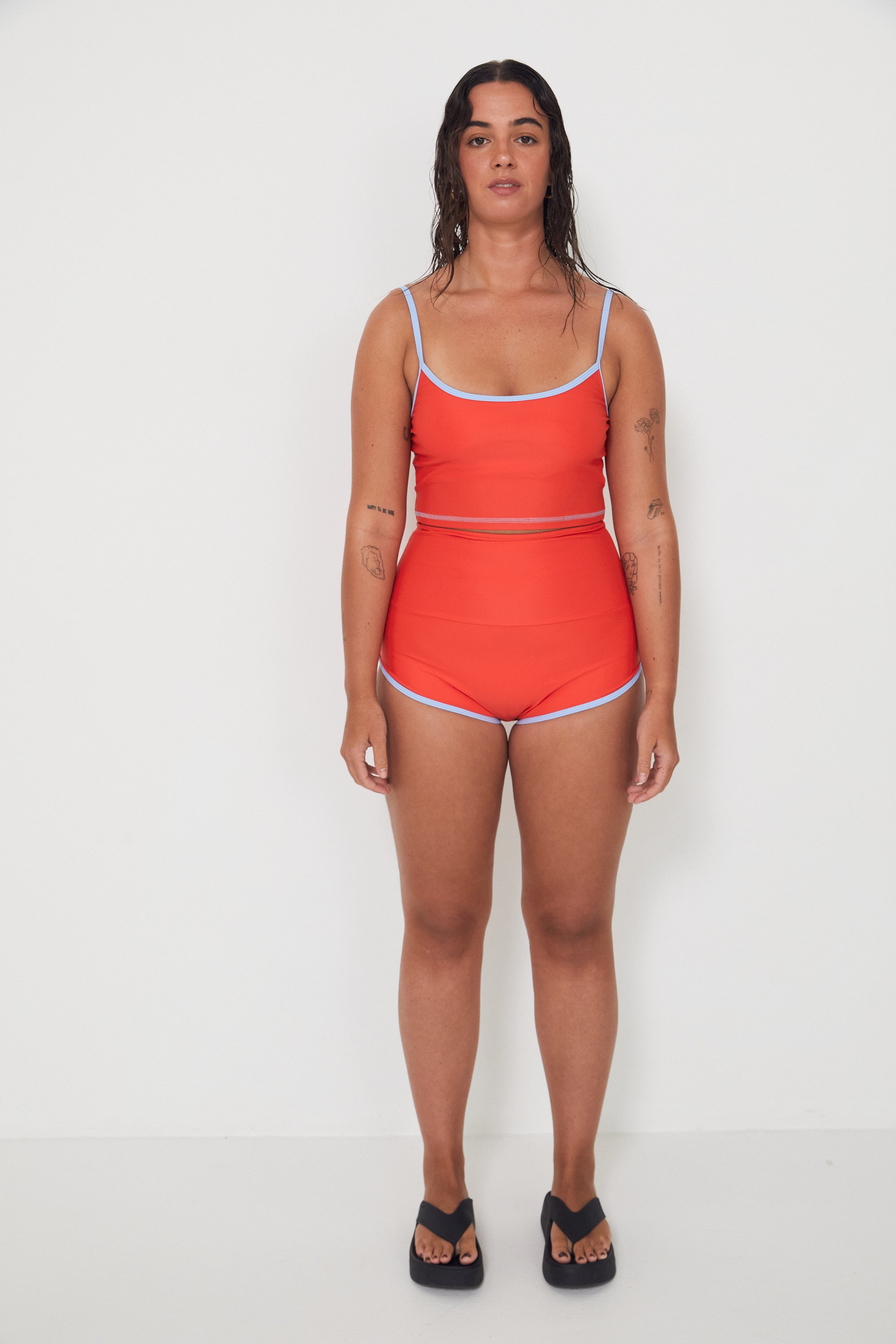 Woman wearing a red tankini surf top and betty bottoms 2.0 with blue trim on a white background