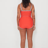 Woman wearing a red tankini surf top and betty bottoms 2.0 with blue trim on a white background