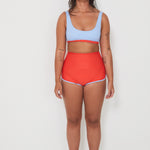 Woman wearing a light blue sports and swim bra and red swim shorts on a white background