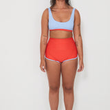 Woman wearing a light blue sports and swim bra and red swim shorts on a white background