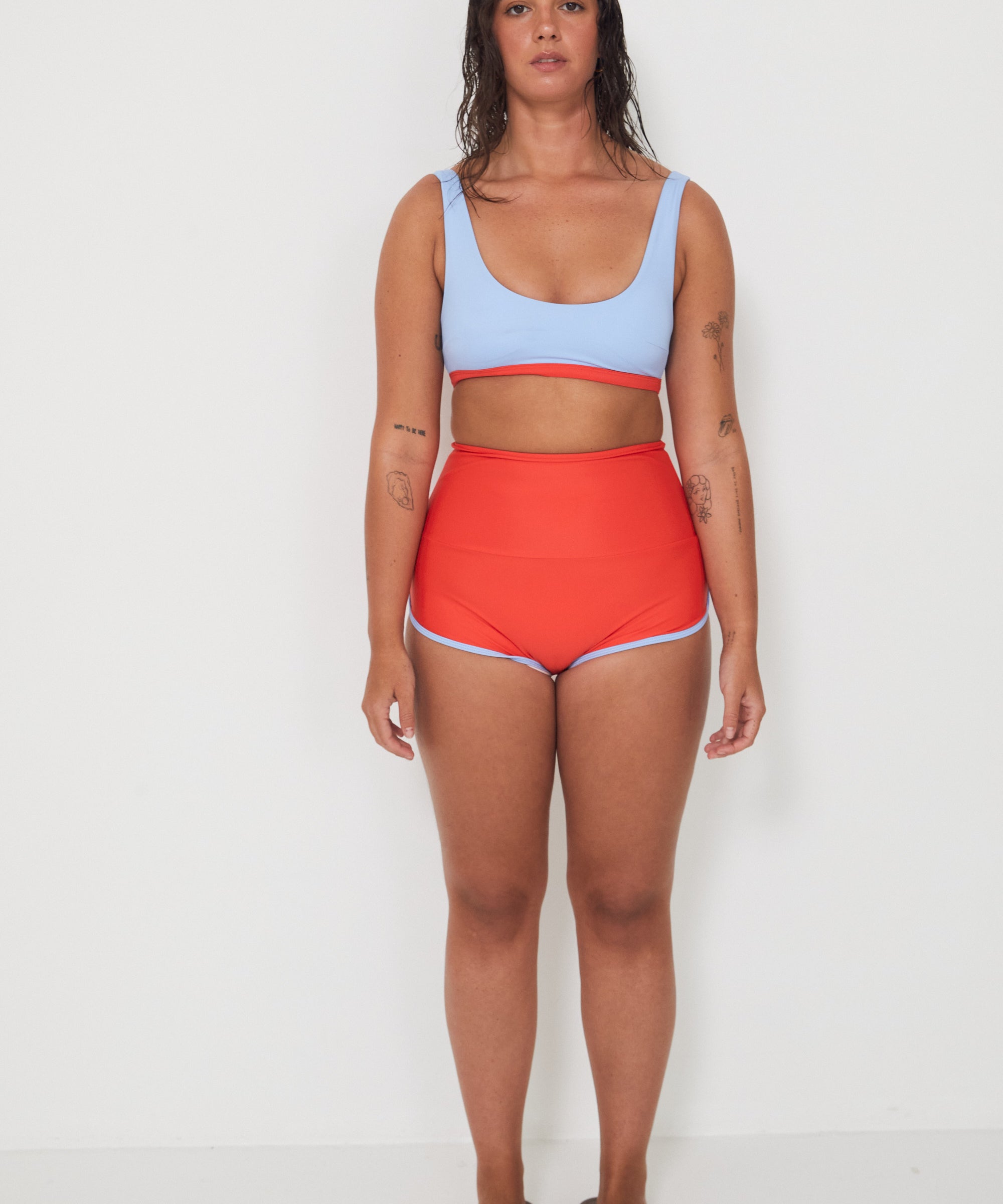 Woman wearing a light blue sports and swim bra and red swim shorts on a white background