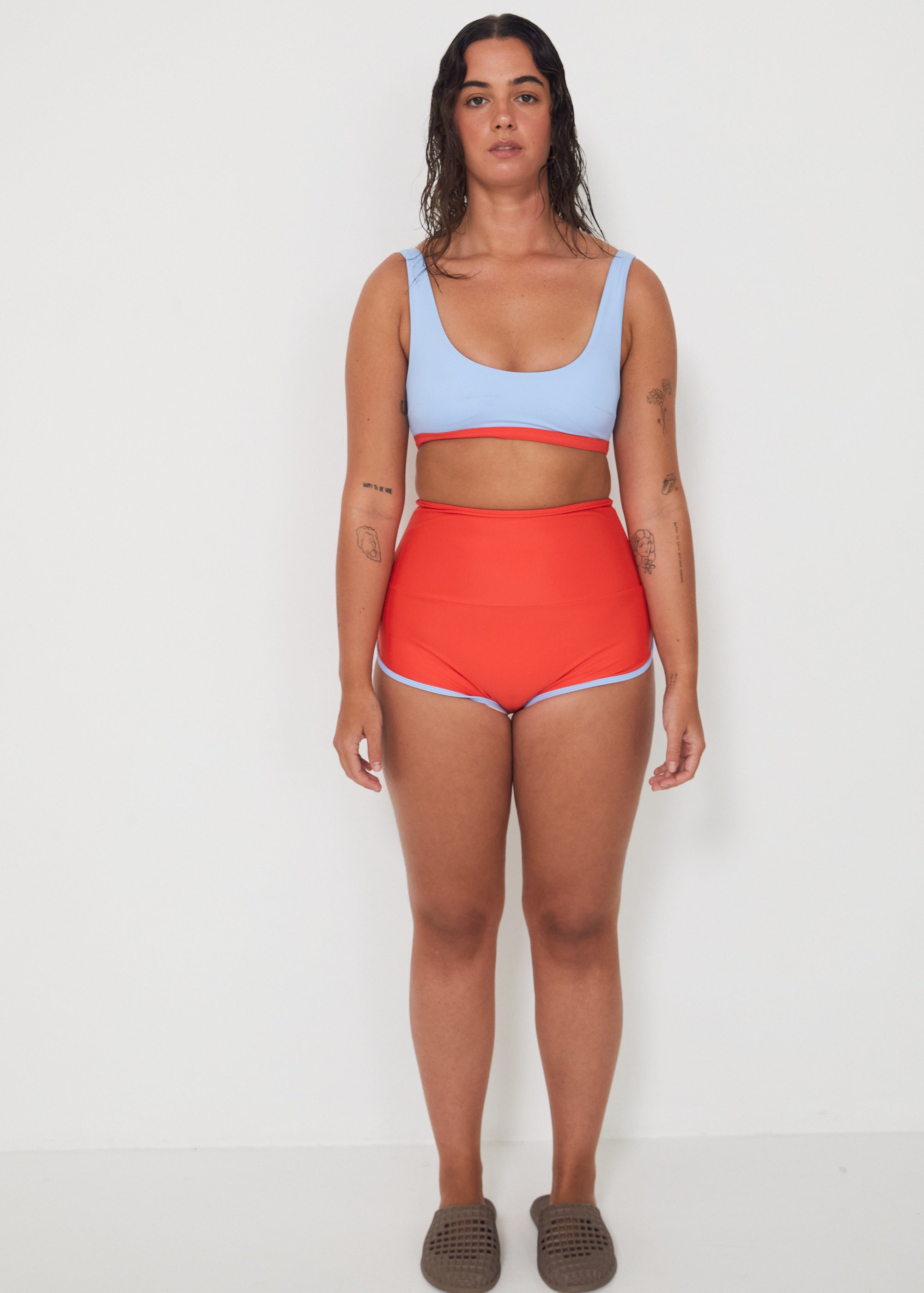 Woman wearing a light blue sports and swim bra and red swim shorts on a white background