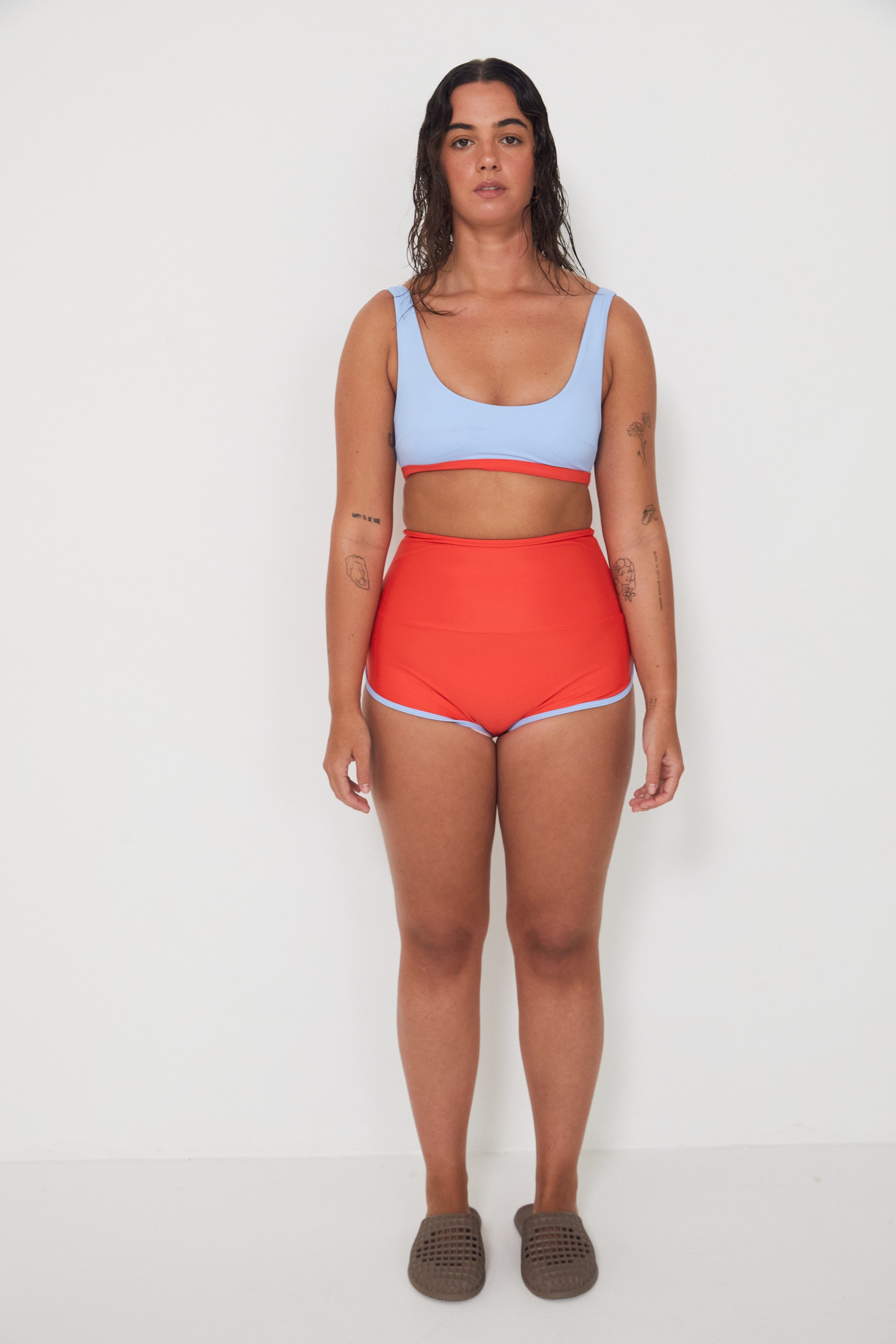 Woman wearing a light blue sports and swim bra and red swim shorts on a white background
