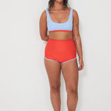 Woman wearing a light blue sports swim bralette and red swim shorts on a white background
