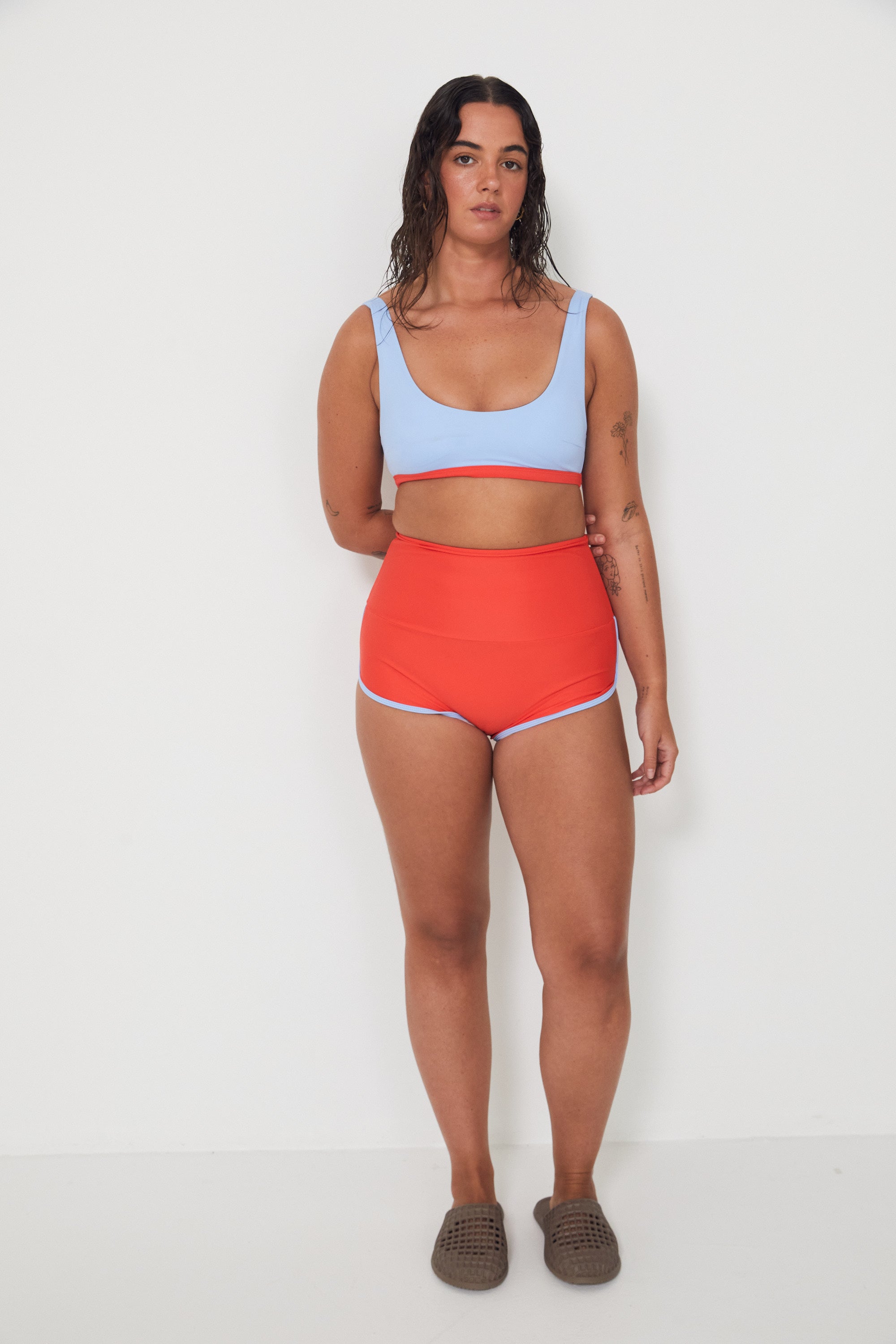Woman wearing a light blue sports swim bralette and red swim shorts on a white background