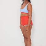 Woman wearing a light blue sports and swim bra and red swim shorts on a white background