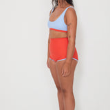 Woman wearing a light blue sports and swim bra and red swim shorts on a white background