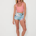 Woman wearing a red and white checkered punchy surf top and patterned original betty bottoms shorts on a white background
