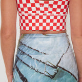 Person wearing a red and white checkered punchy surf crop top and blue shorts with graphic design.
