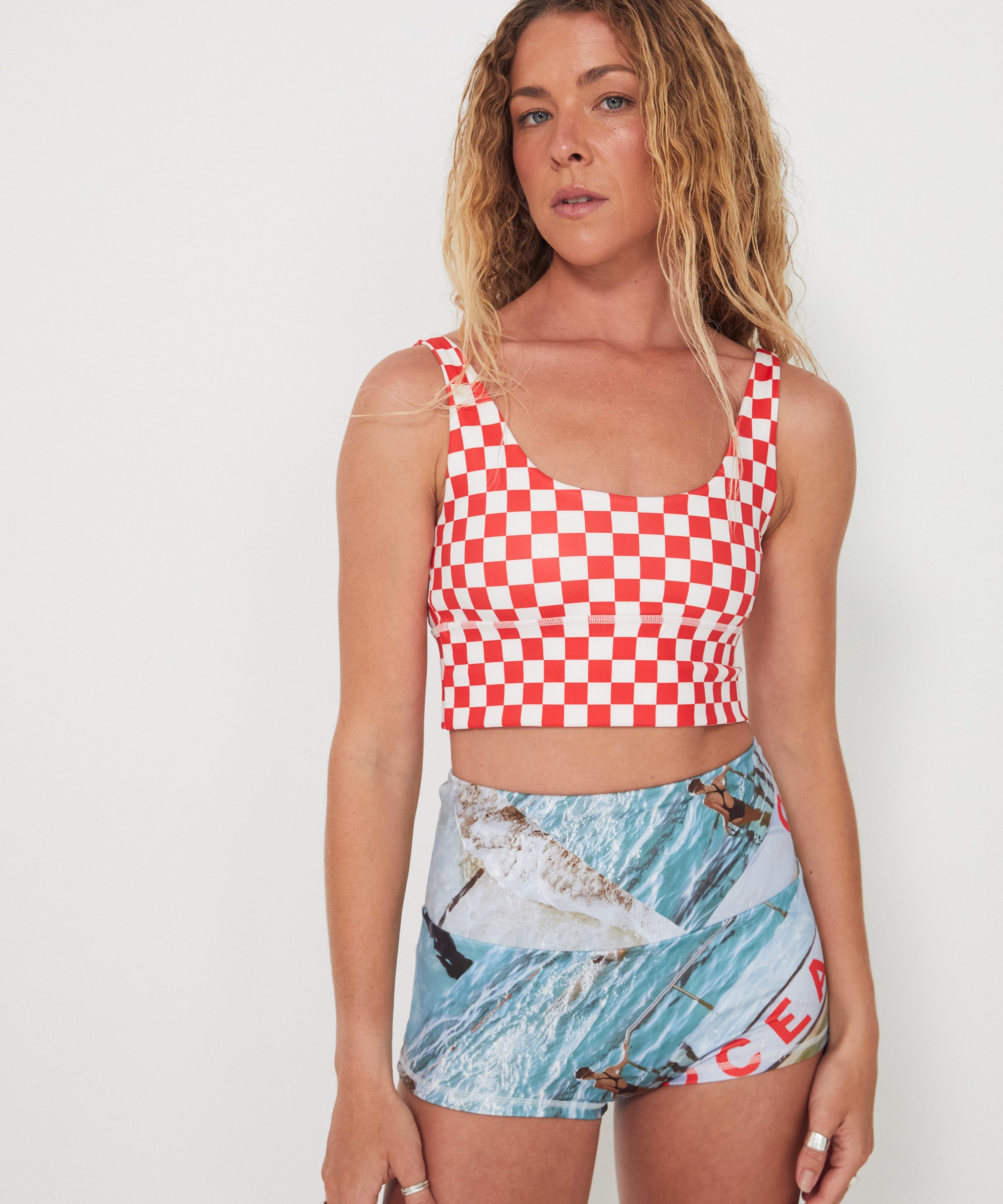 Woman wearing a red and white checkered punchy surf top and patterned ocean photographed shorts on a white background