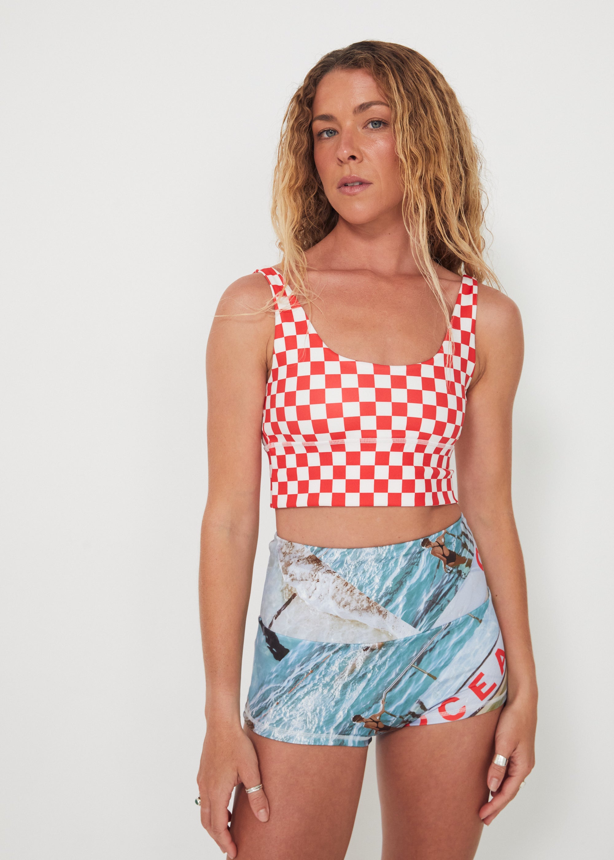 Woman wearing a red and white checkered punchy surf top and patterned ocean photographed shorts on a white background