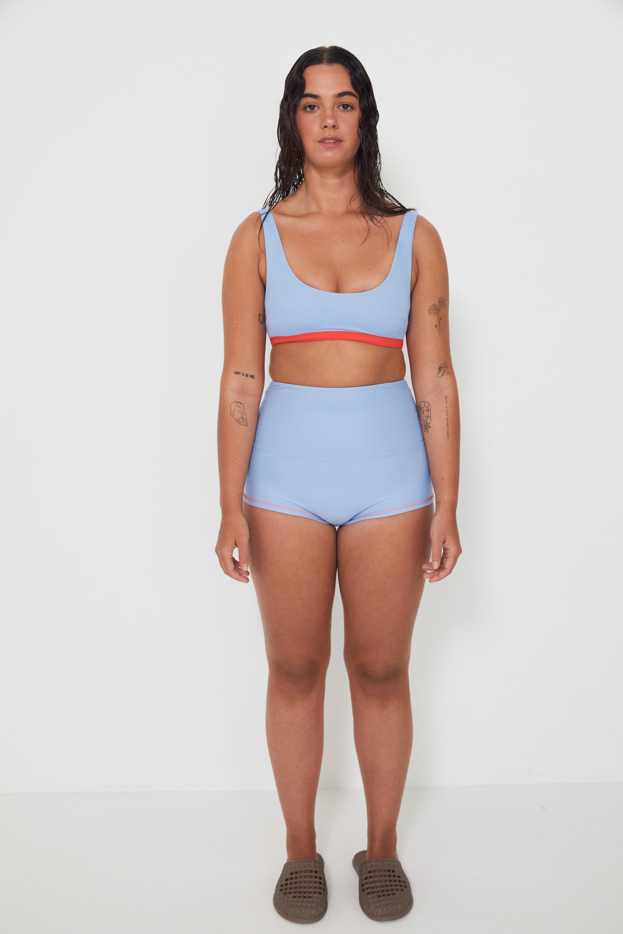 Woman wearing a light blue bralette bikini and original betty bottoms with a white background