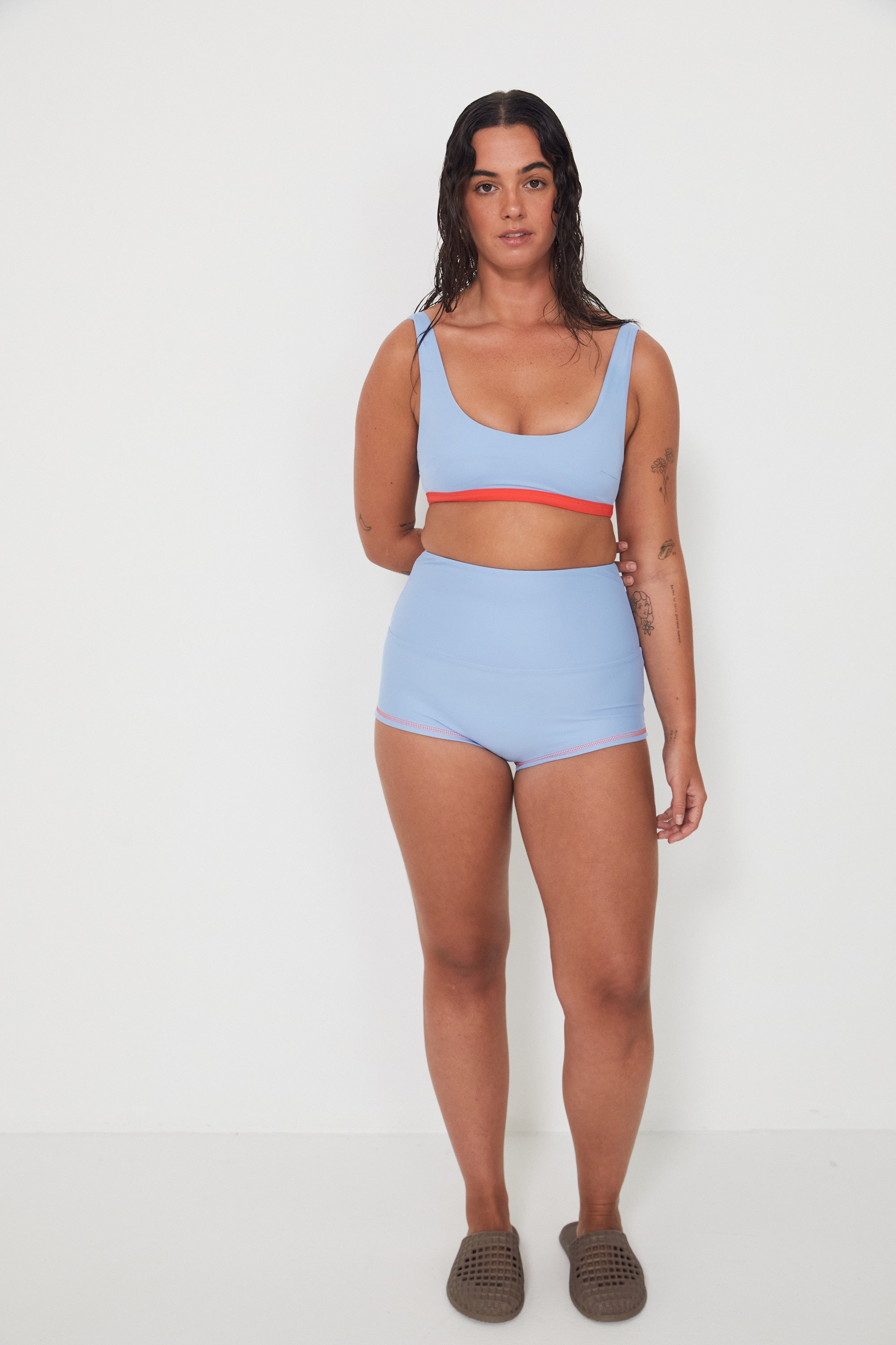 Woman wearing a light blue bralette surf top and high-waisted original betty bottom shorts on a white background