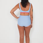 Person wearing a light blue sports bralette surf top bra and high-waisted original betty bottoms swim bottoms on a white background