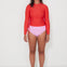 Woman wearing a red long-sleeve  ruched rashguard, salt gypsy swimwear top and pink high-waisted bikini drifter bottoms on a white background, ready for a beach swim