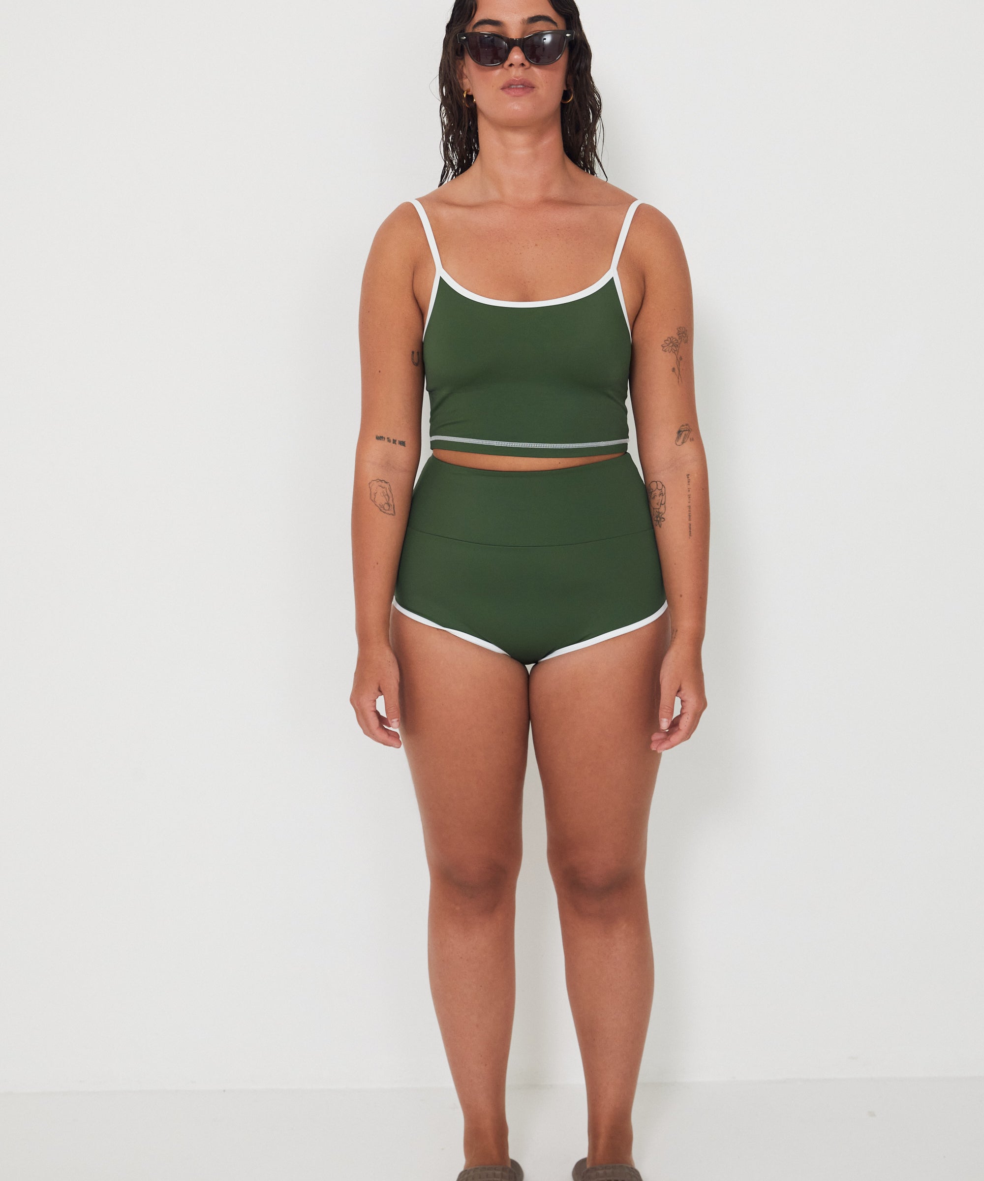 Woman wearing a green tankini surf top and betty bottoms 2.0 swimsuit with white trim against a white background