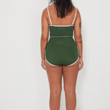 Woman wearing a green tankini surf top and betty bottoms 2.0 swimsuit with white trim from the back against a white background