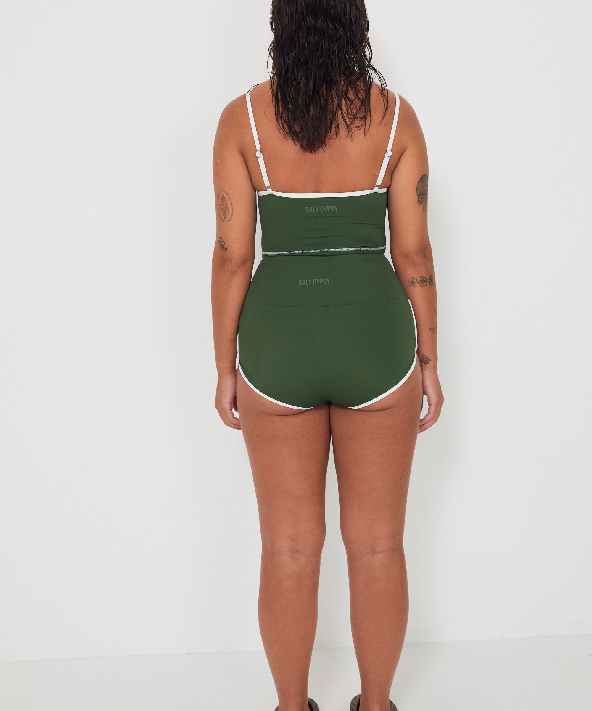 Woman wearing a green tankini surf top and betty bottoms 2.0 swimsuit with white trim against a white background