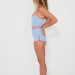 Woman wearing a baby blue tankini surf top and betty bottoms 2.0 with red trim on a white background