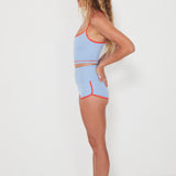 Woman wearing a baby blue tankini surf top and betty bottoms 2.0 with red trim on a white background