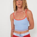Woman wearing a light blue tankini surf top bra and red boarshorts on a white background