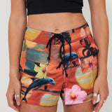 Woman wearing a black tankini surf top and colorful floral and vacay print boardshorts by salt gypsy and friday on a white background