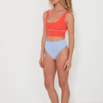 Woman wearing a red punchy bikini top and light blue high-waisted reversible drifter bottoms on a white background