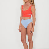 Woman wearing a red punchy bikini top and light blue high-waisted reversible drifter bottoms on a white background