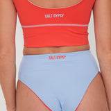 Person wearing a red 'Salt Gypsy' punchy surf bikini top and light blue drifter bottoms on a plain background