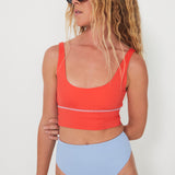 Woman wearing an red punchy bikini top and light blue reversible drifter bottoms against a white background