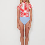 Person wearing a red and white checkered rashguard and light blue high-waisted bottoms on a white background