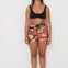 Woman wearing a black bralette swimwear crop top and vacay floral holiday swimwear boardshorts on a white background collaboration of salt gypsy and friday 