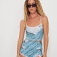 Woman wearing a blue and white patterned swim set with sunglasses on a plain background