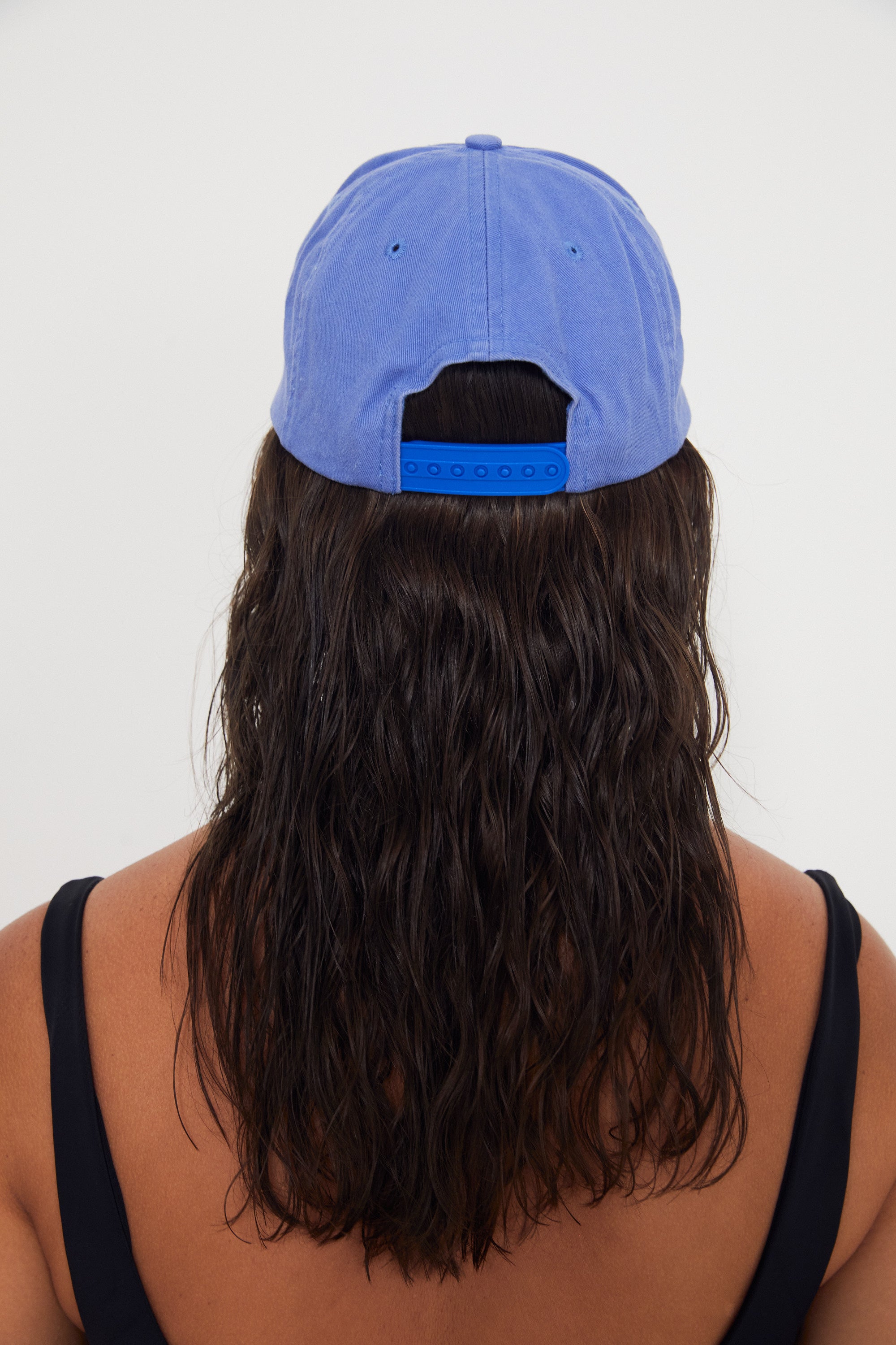 Person wearing a blue dad cap from behind on a white background