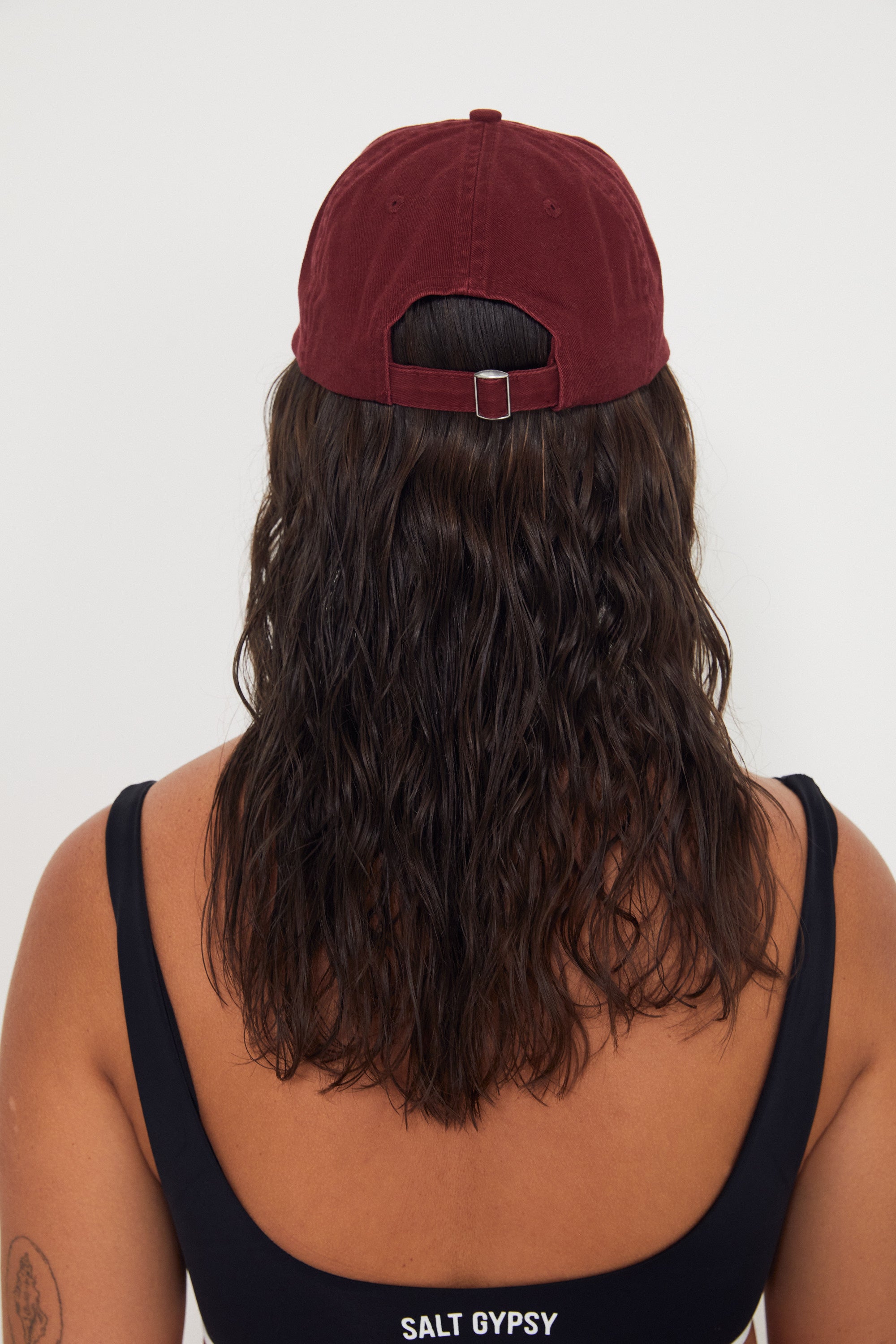 Person wearing a maroon cap and black tank top with 'Salt Gypsy' branding on a white background