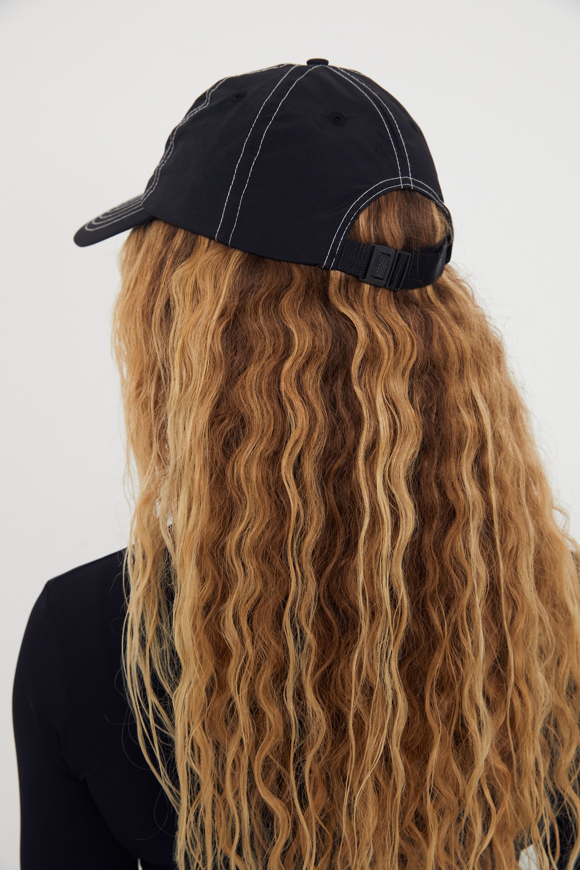 Person wearing a black nylon cap with long wavy hair on a white background