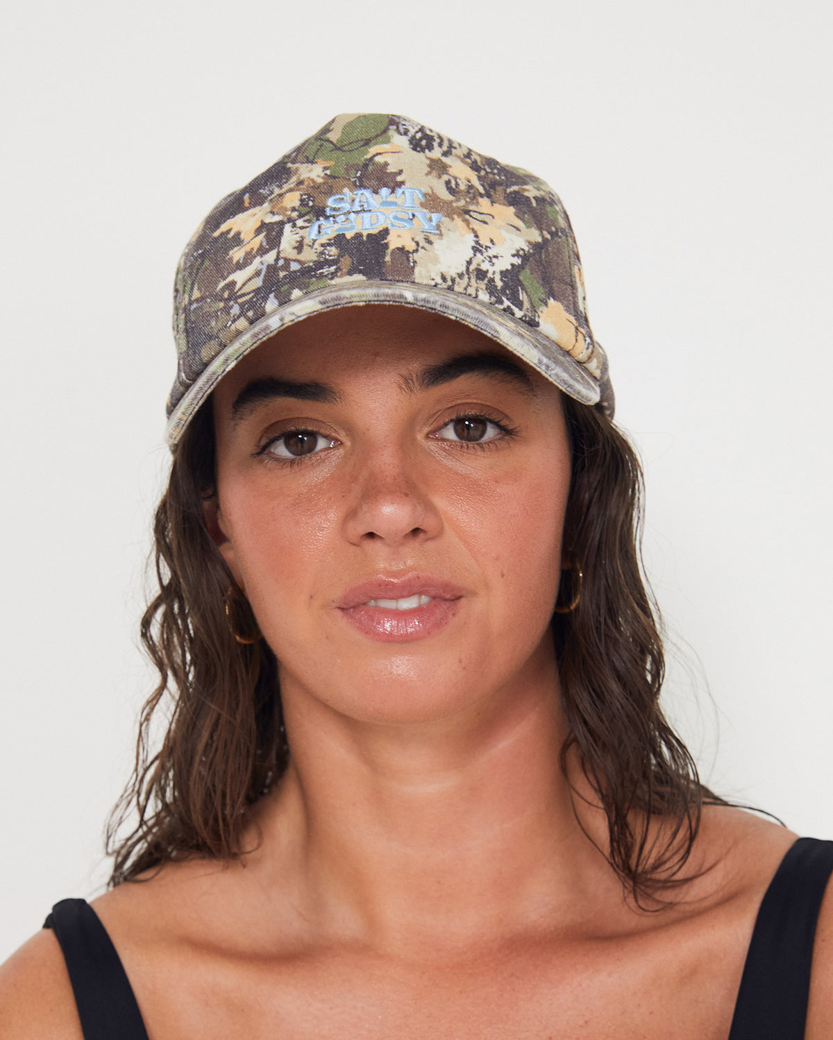 women wearing a camouflage dad cap with blue embroidered salt gypsy text on a plain background