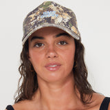 women wearing a camouflage dad cap with blue embroidered salt gypsy text on a plain background